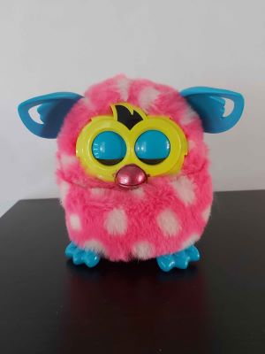 A very round pink Furby boom! with white spots. Her plastic ears and feet are blue and she has a shiny pink beak that looks like it's gotten a nail polish treatment.