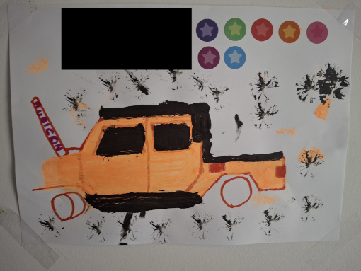 A painting of a Jeep Wrangler Rubicon in orange (meant to approximate a tan colour) with its bonnet open and some creative use of black paint to indicate depth. There are a number of star stickers on the painting because he was really feeling himself with this one. Yes, it is taped up on our wall.